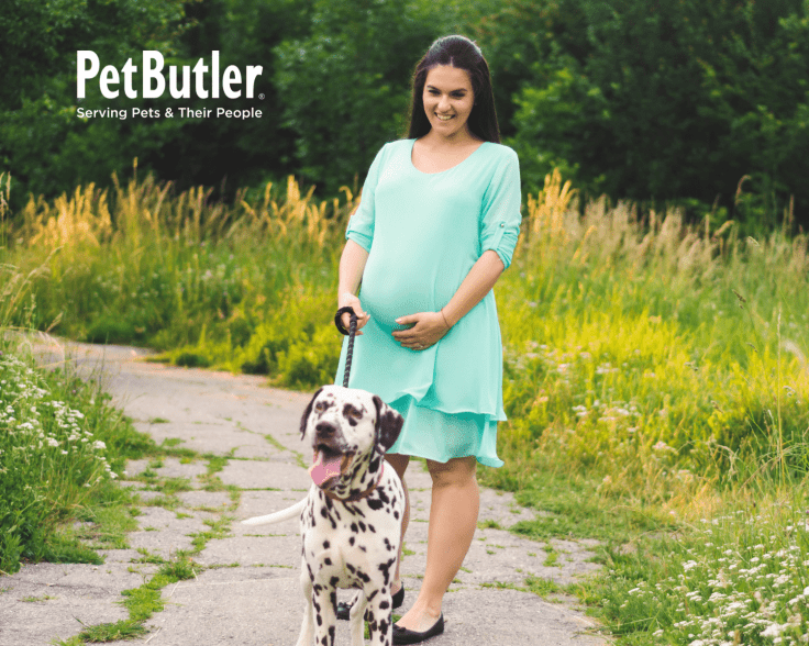 Pregnant woman wearing a teal dress walking her dog along a trail, holding her belly.