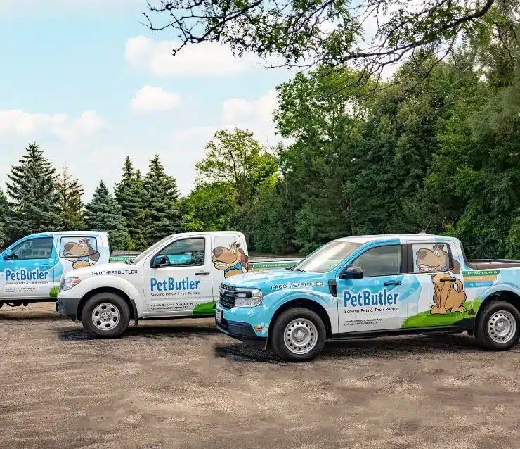 Three logoed Pet Butler pick up trucks parked next to each other with tall trees in the background.